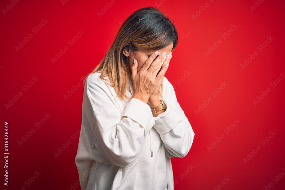 Middle age beautiful sportswoman wearing casual sweatshirt over isolated red background with sad expression covering face with hands while crying. Depression concept. Middle age beautiful sportswoman wearing casual sweatshirt over isolated red background with sad expression covering face with hands while crying. Depression concept.