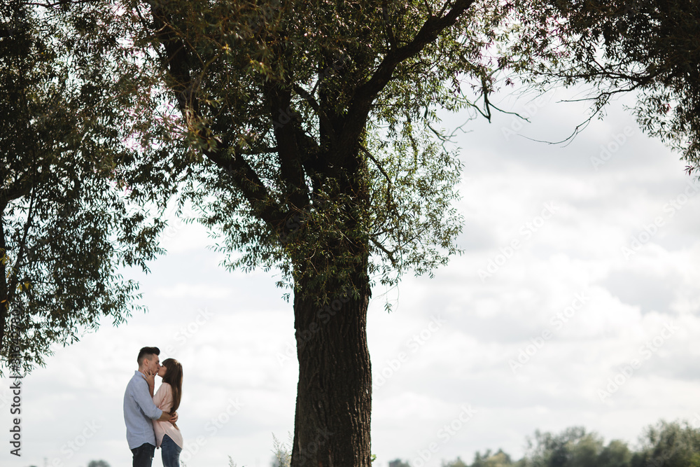 Young romantic couple is having fun in summer sunny day near the lake. Enjoying spending time together in holiday. Man and woman are hugging and kissing. Young romantic couple is having fun in summer sunny day near the lake. Enjoying spending time together in holiday. Man and woman are hugging and kissing.