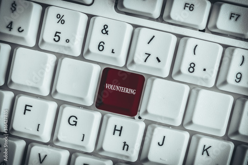 Text sign showing Volunteering. Business photo text Provide services for no financial gain Willingly Oblige White pc keyboard with empty note paper above white background key copy space photo