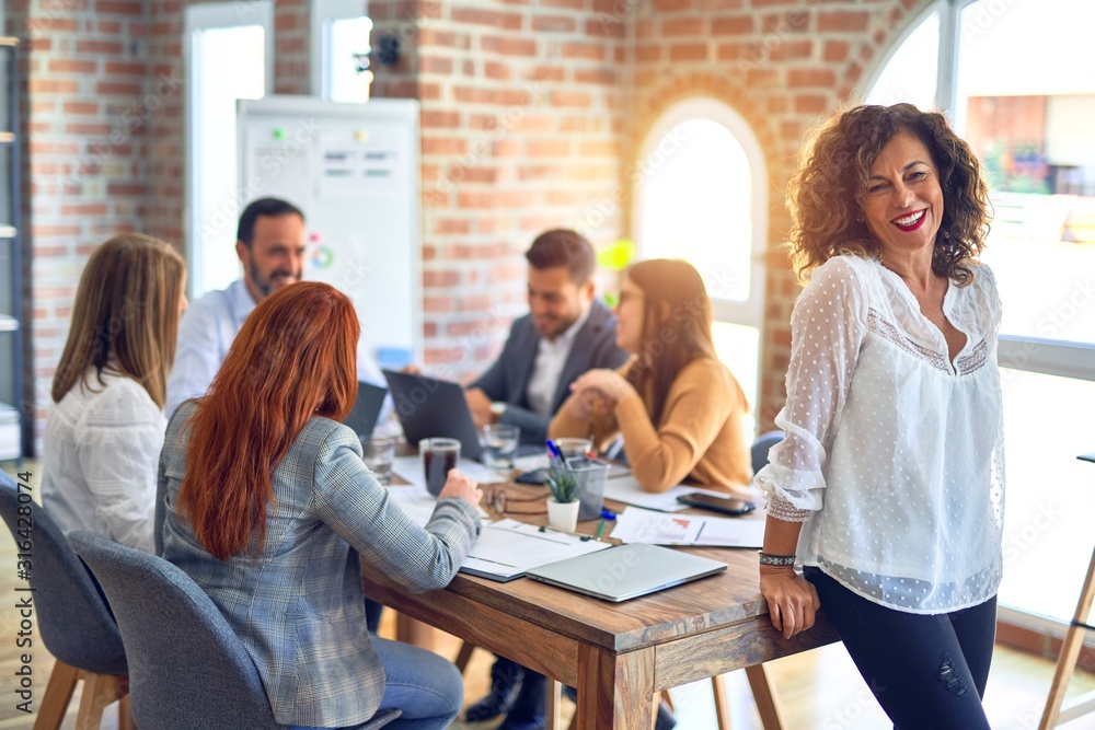 Group of business workers working together. Middle age beautiful businesswoman standing smiling happy looking at the camera at the office Group of business workers working together. Middle age beautiful businesswoman standing smiling happy looking at the camera at the office