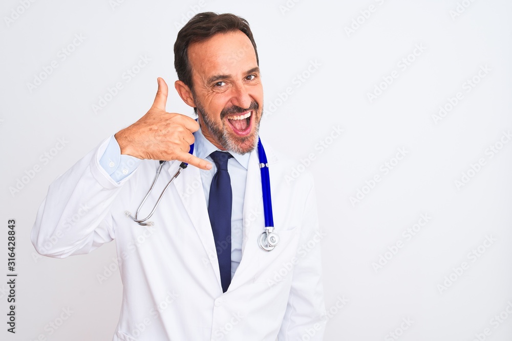 Middle age doctor man wearing coat and stethoscope standing over isolated white background smiling doing phone gesture with hand and fingers like talking on the telephone. Communicating concepts. Middle age doctor man wearing coat and stethoscope standing over isolated white background smiling doing phone gesture with hand and fingers like talking on the telephone. Communicating concepts.