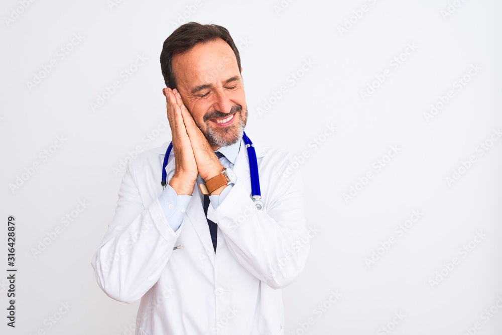 Middle age doctor man wearing coat and stethoscope standing over isolated white background sleeping tired dreaming and posing with hands together while smiling with closed eyes. Middle age doctor man wearing coat and stethoscope standing over isolated white background sleeping tired dreaming and posing with hands together while smiling with closed eyes.