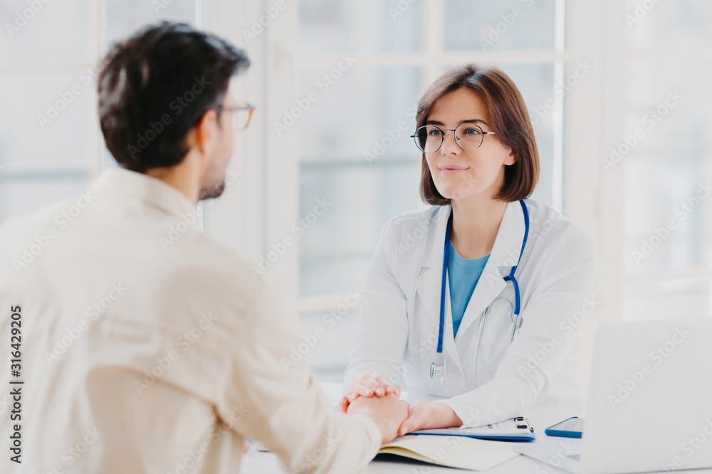 Male patient has consultation with female doctor, receives support, finds out about serious disease. Woman therapist comforts ill visitor in office or consulting room, talk about how to cure illness Male patient has consultation with female doctor, receives support, finds out about serious disease. Woman therapist comforts ill visitor in office or consulting room, talk about how to cure illness