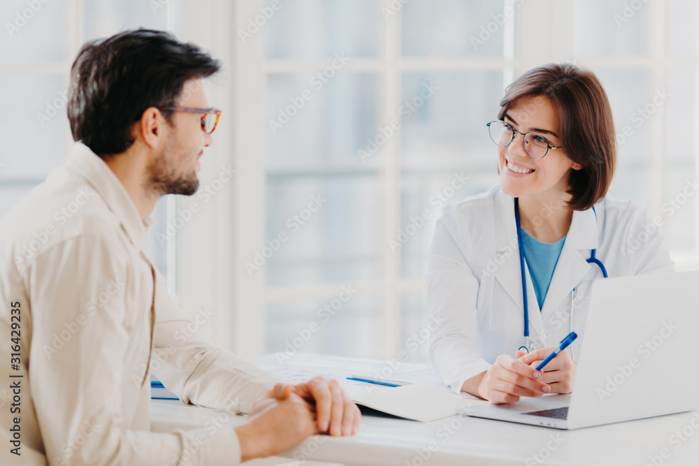 Skilled professional female general practitionist explains diagnosis and consults patient, demonstrates information in laptop, pose in clinical office, discuss scan results in diagnostic center Skilled professional female general practitionist explains diagnosis and consults patient, demonstrates information in laptop, pose in clinical office, discuss scan results in diagnostic center