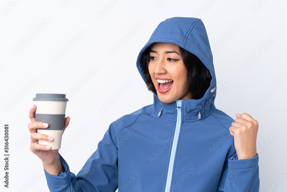 Mixed race woman wearing winter clothes with the hood on and holding a hot takeaway coffee over isolated white background celebrating a victory Mixed race woman wearing winter clothes with the hood on and holding a hot takeaway coffee over isolated white background celebrating a victory