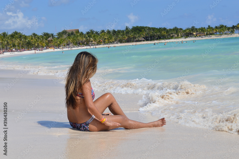 Pretty young woman with highlights is sitting on white sand beach and looking at a waves in Riviera Maya, Mexico. Pretty young woman with highlights is sitting on white sand beach and looking at a waves in Riviera Maya, Mexico.