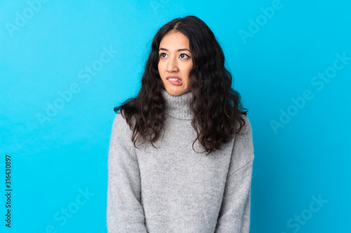Spanish Chinese woman over isolated blue background with confuse face expression