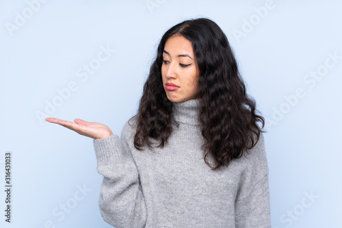 Spanish Chinese woman over isolated blue background holding copyspace with doubts