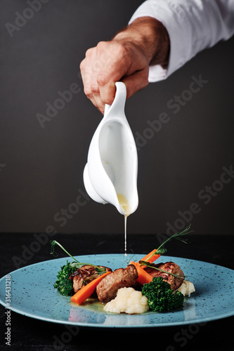 Chef pouring a gravy or sauce over the meat salad