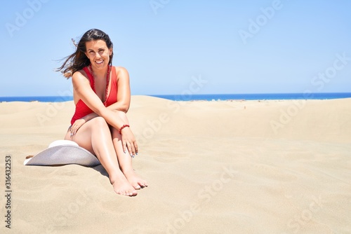 Young beautiful woman sunbathing sitting on the sand wearing summer swinsuit at maspalomas dunes bech
