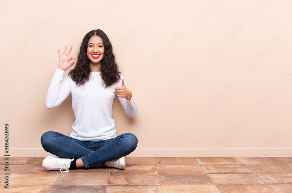 Young woman sitting on the floor showing ok sign and thumb up gesture