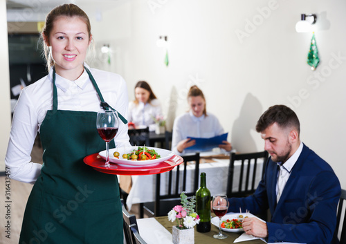 Affable female waiter is standing with order in luxury restaurante