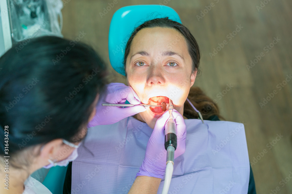 Dentist and patient in dentist office. Close-up of dental drill use for patient teeth in dentistry office in a dental treatment procedure. Woman having teeth examined at dentists Dentist and patient in dentist office. Close-up of dental drill use for patient teeth in dentistry office in a dental treatment procedure. Woman having teeth examined at dentists