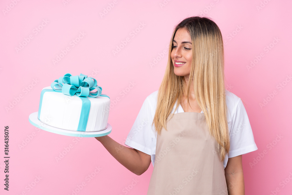 Young Uruguayan pastry woman with a big cake over isolated pink background with happy expression Young Uruguayan pastry woman with a big cake over isolated pink background with happy expression