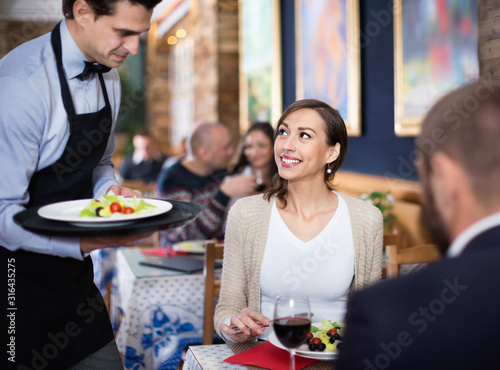 Waiter with dishes serving man and woman friendly company indoors