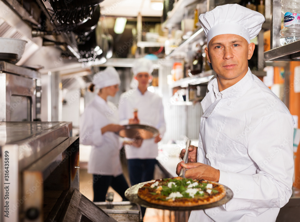 Confident chef getting pizza out of oven