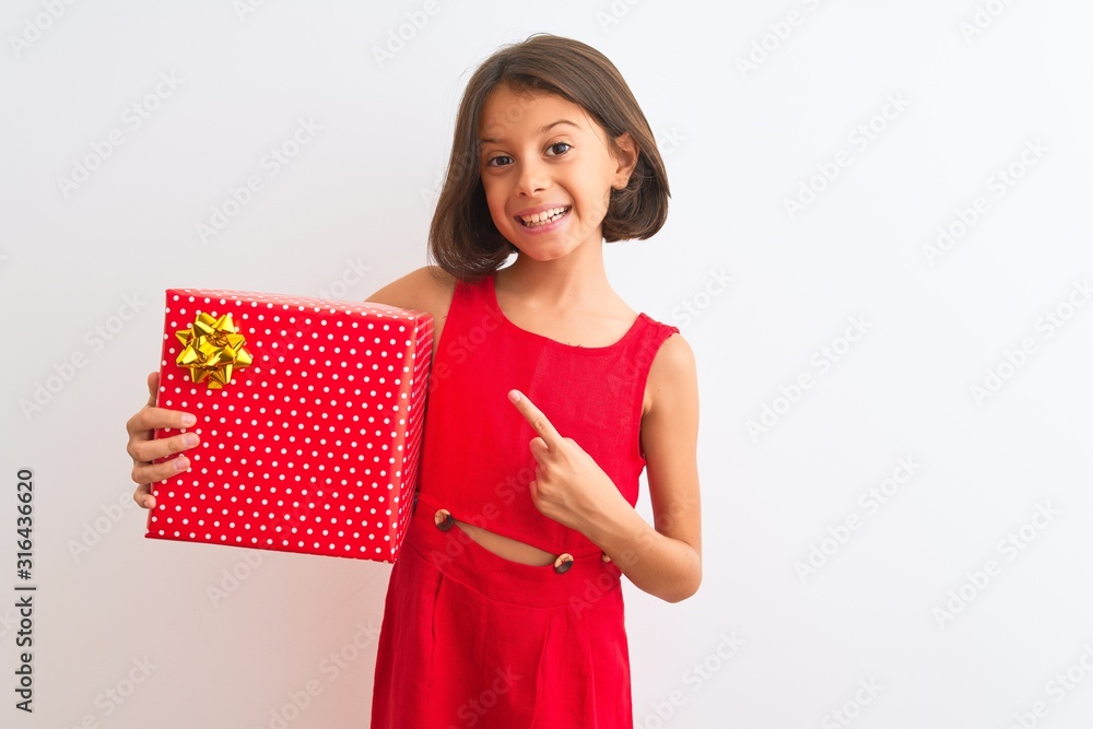 Beautiful child girl holding birthday gift standing over isolated white background very happy pointing with hand and finger Beautiful child girl holding birthday gift standing over isolated white background very happy pointing with hand and finger