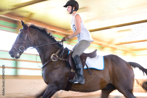 Female rider landing a jump during riding lessons in indoor arena