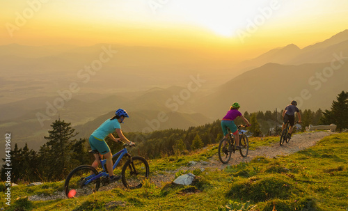 Canvas-taulu LENS FLARE: Four young travelers ride their mountain bikes downhill at sunrise