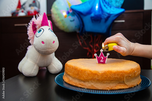 Homemade cake with candle, unicorn plush toy on balloons background