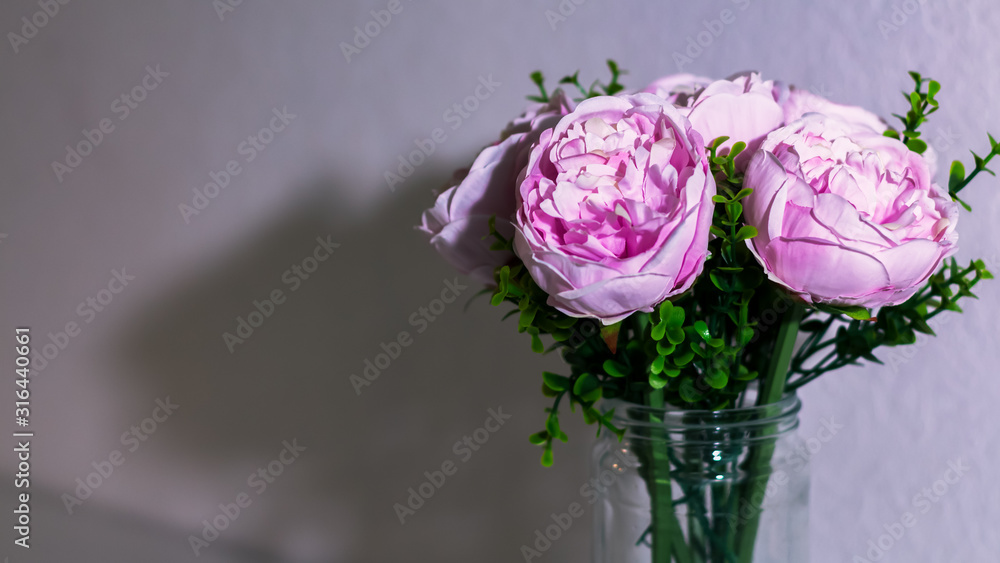 Ramo de flores artificiales en un florero de vidrio. Luz directa blanca sobre el ramo y fondo de pared blanca. Ramo de flores aislado. Ramo de flores artificiales en un florero de vidrio. Luz directa blanca sobre el ramo y fondo de pared blanca. Ramo de flores aislado.