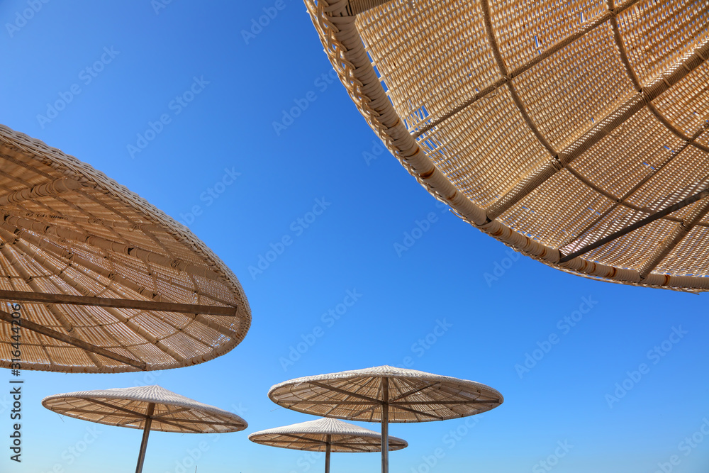 Tropical beach sun shades against bright blue sky on a sunny day. Up view. Sun umbrellas of reed and straw. Travel and vacation. Background with copy space