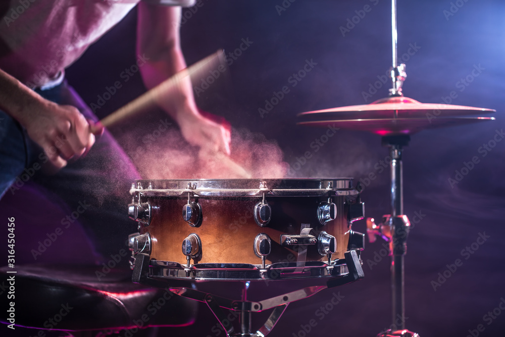Naklejka premium The drummer plays the drums. Beautiful blue and red background, with rays of light. Beautiful special effects smoke and lighting. The process of playing a musical instrument.
