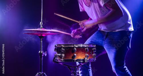 A drummer plays drums on a blue background. Beautiful special effects of light and smoke. The process of playing a musical instrument.