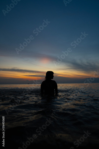 Silueta de mujer en la orilla del mar con el atardecer de fondo