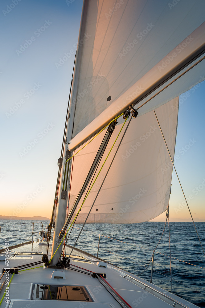 Obraz premium Chasing the sun at sailing yacht. Deck and sails of sailoat pointing to the sunrise. Mediterranean sea, Italy.