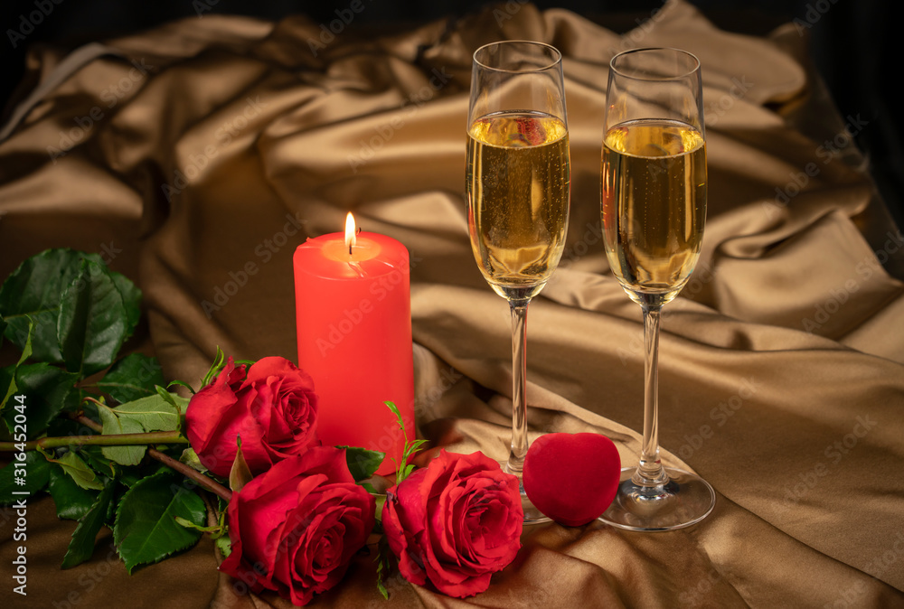 Valentine's day card, two glasses of champagne on a gold background red roses and a red heart, a lighted candle Valentine's day card, two glasses of champagne on a gold background red roses and a red heart, a lighted candle