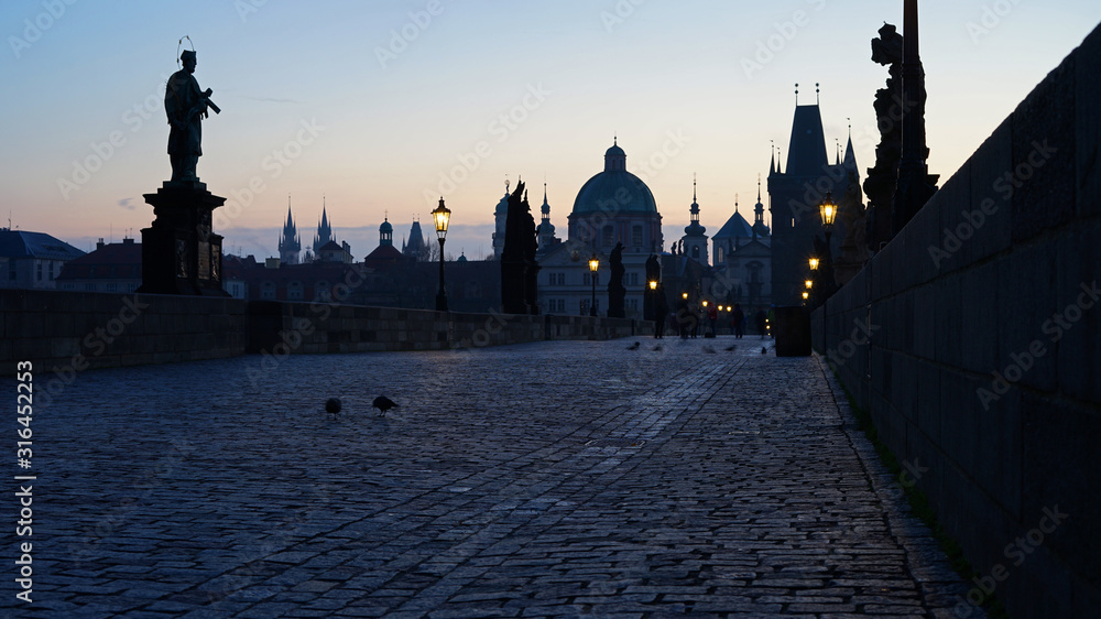 Sunrise at famous historic Charles Bridge with lit lamps and statues, Prague, Czech Republic