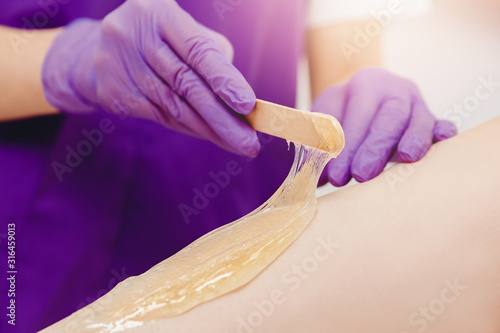Application of sugar paste for shugaring depilation with scraper on skin of girl legs. Hair removal concept photo