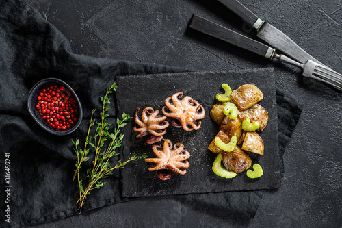 Roasted octopus. Baked potatoes and celery. Black background. Top view