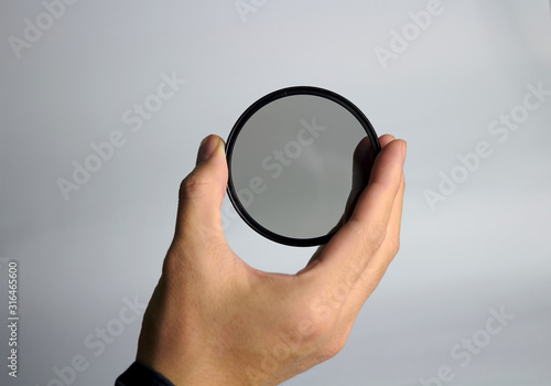 Fotografi Hand holds ND lens camera filter on white background