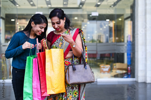 Mother and adult daughter posing together outside the shopping mall after shopping for festive season with colorful shopping bags in hand.