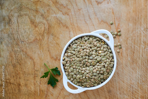 Raw green lentils in a white bowl on a wooden background 