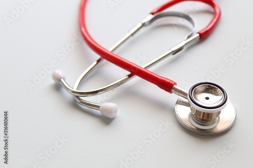 Red stethoscope on a grey background.This is an acoustic medical device for auscultation, or listening to the internal sounds of an animal or human body such as the heart or lungs.