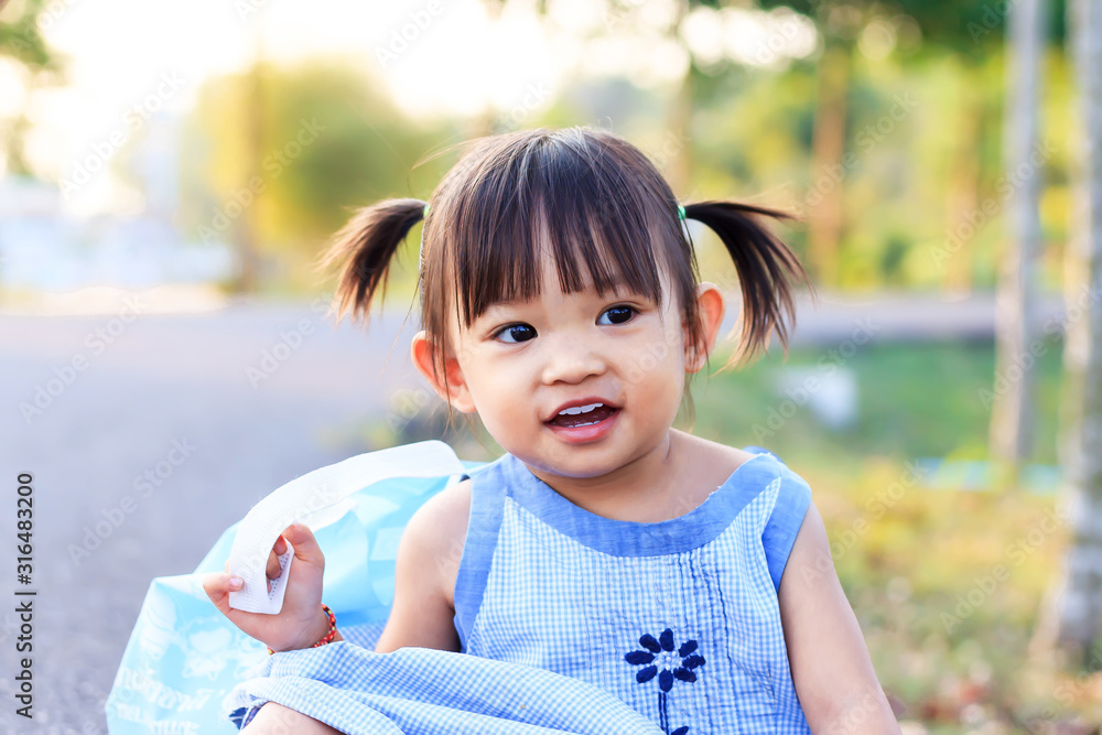 Portrait image of 1 2 years old baby. Happy Asian child girl smiling and relaxing at the garden park. Pretty girl wearing a blue dress. Summer season. Kids and travel concept. Stock