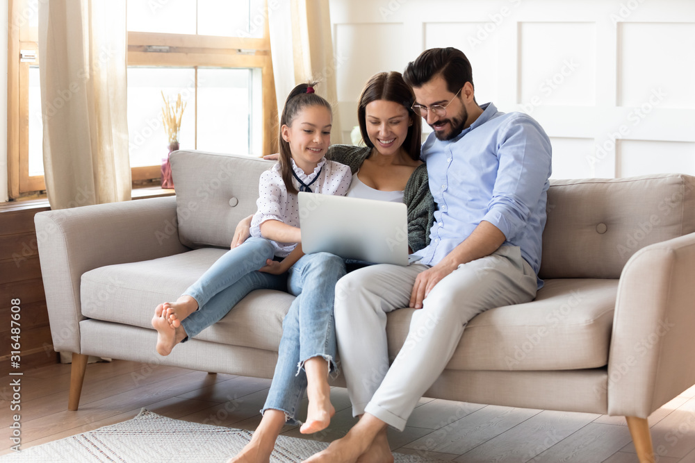 Happy parents with little daughter use laptop at home