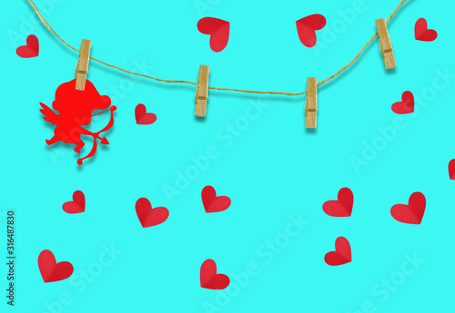 The Valentine's day concept.The red cupid shaped card attached to a wooden clip Hanging with hemp rope on blue background.Valentine's Day background