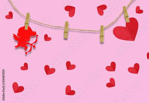 The Valentine's day concept.The red cupid shaped card attached to a wooden clip Hanging with hemp rope on pink background.Valentine's Day background
