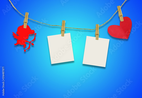 Valentine's day concept.Red cupid shaped card attached to a wooden clip Hanging with hemp rope on blue background.Valentine's Day background