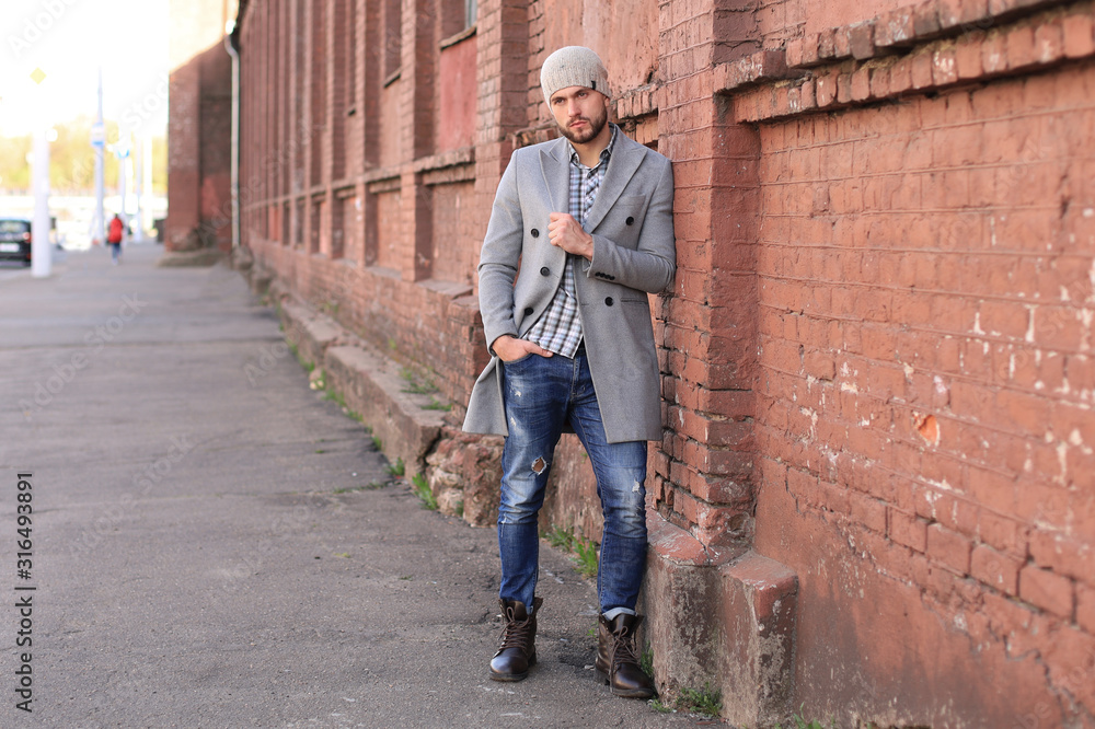 City life. Stylish young man in grey coat and hat standing on the street in the city. City life. Stylish young man in grey coat and hat standing on the street in the city.
