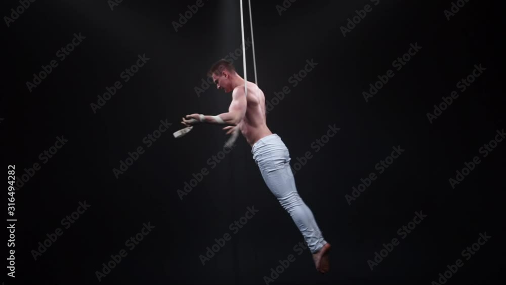 Muscular circus aerialist on the aerial straps in black studio Muscular circus aerialist on the aerial straps in black studio