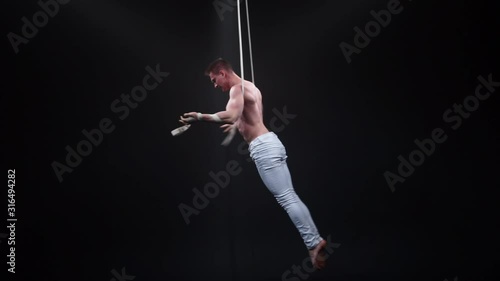 Muscular circus aerialist on the aerial straps in black studio photo