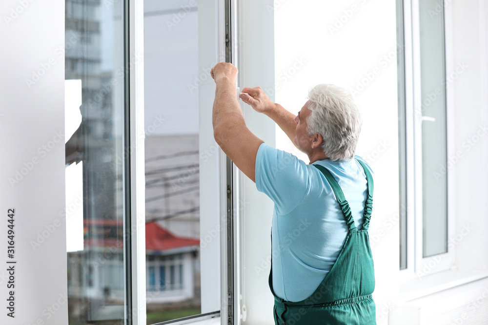 Mature construction worker repairing plastic window indoors Mature construction worker repairing plastic window indoors