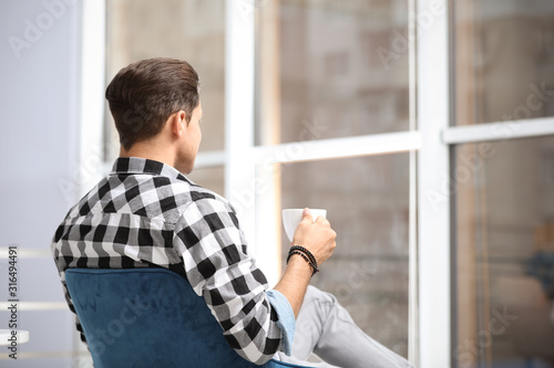 Man with cup of drink resting near window at home