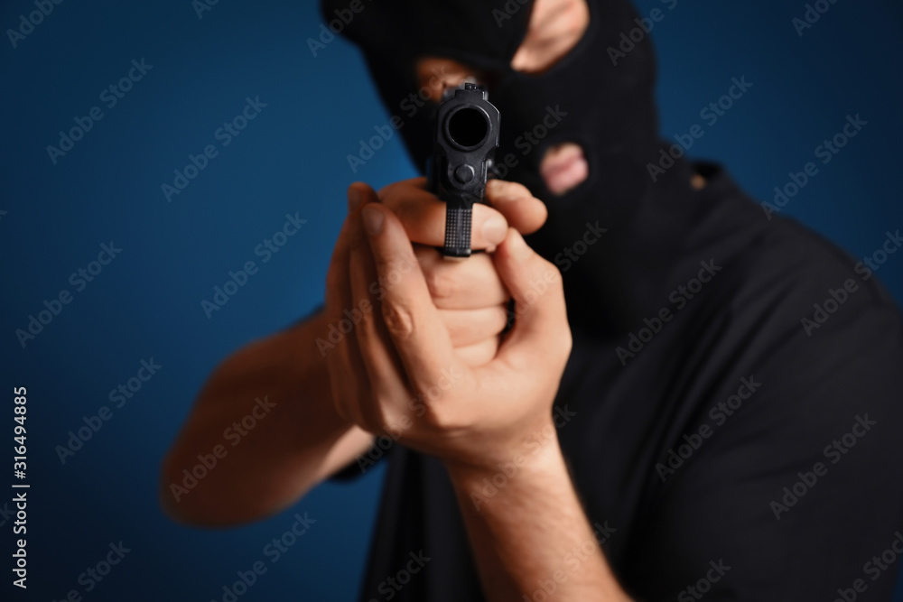 Man in mask holding gun against dark blue background, focus on hands Man in mask holding gun against dark blue background, focus on hands