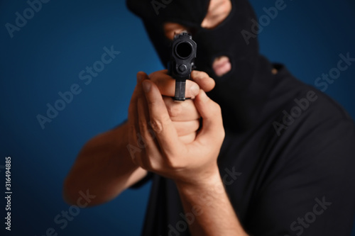 Man in mask holding gun against dark blue background, focus on hands
